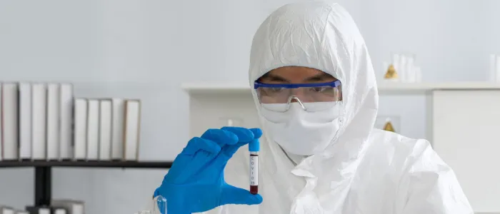Researcher in full PPE hazmat suit holding a medical test tube for chemical safety analysis.
