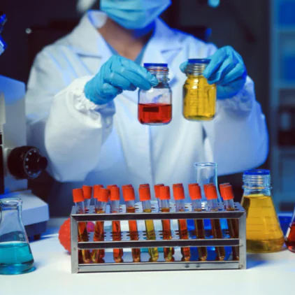Close-up of a laboratory scientist in blue gloves holding a round bottom glass flask with yellow chemical solution – Saffron Chemicals UAE