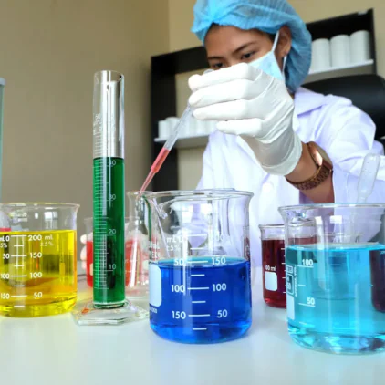 Laboratory scientist in protective blue gloves holding a round bottom flask with yellow chemical solution – Saffron Chemicals UAE